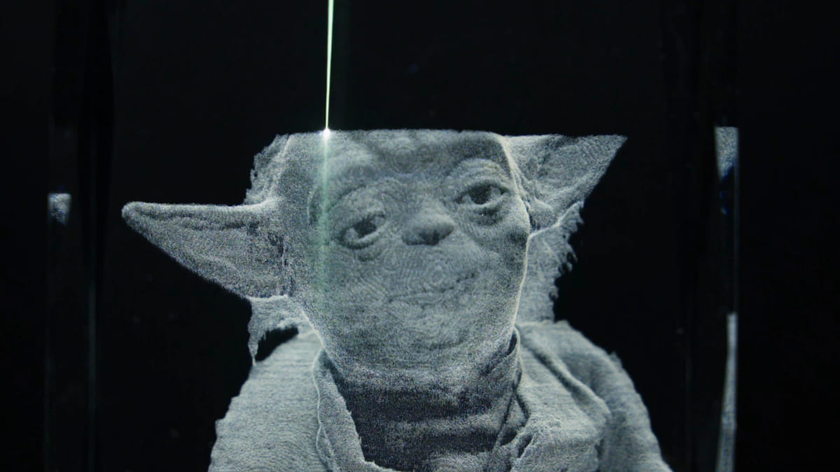 A figurine etched in frosted white inside a clear glass block, with a narrow pale beam track running down through the glass to a bright point on the top of its head.